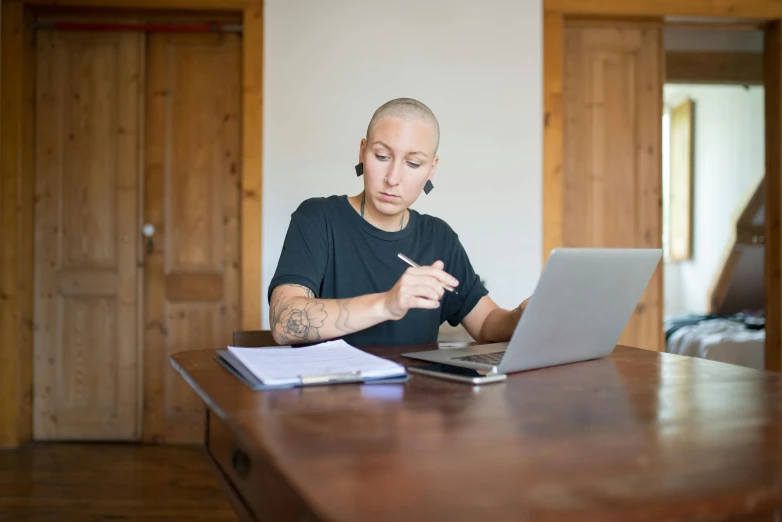 a man sitting at a table working on a laptop, a portrait, by Julia Pishtar, pexels, academic art, buzz cut hair, photograph of a techwear woman, tattooed, 15081959 21121991 01012000 4k