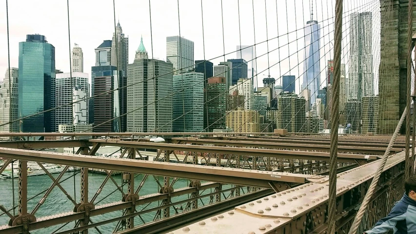 a man standing on top of a bridge next to a river, inspired by Thomas Struth, pexels contest winner, new york skyline, nets, closeup - view, metallic bridge