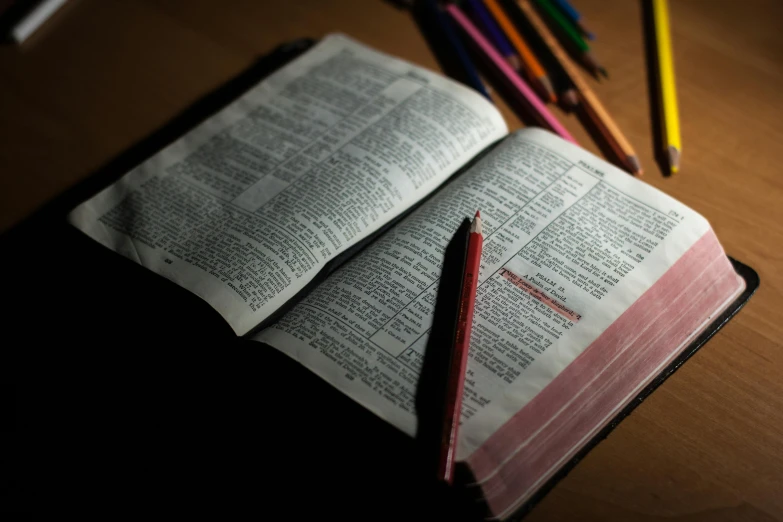 an open bible sitting on top of a wooden table, pexels, red ballpoint pen, with a black background, with a bunch of stuff, thumbnail