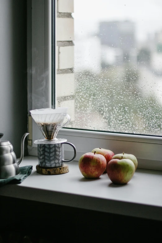 a couple of apples sitting on top of a window sill, a still life, unsplash contest winner, steaming coffee, rain sensor, grey, pouring