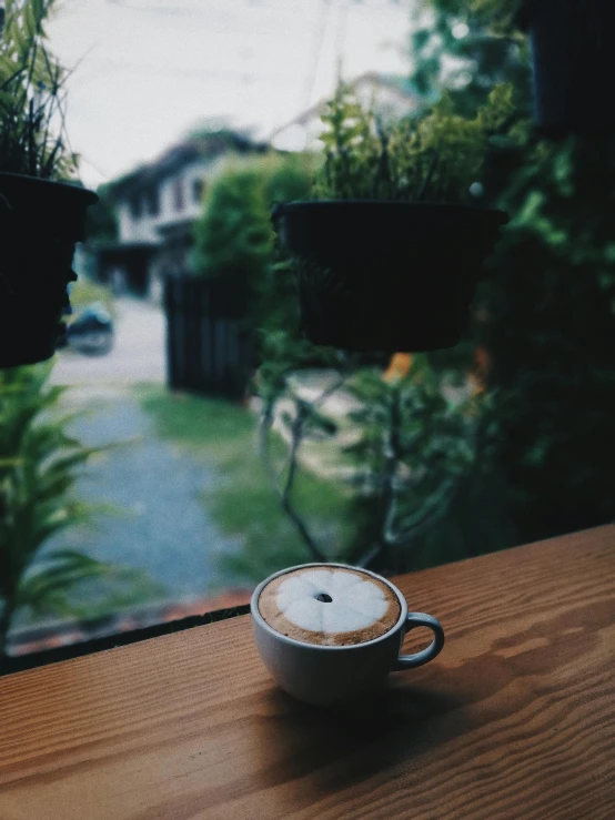 a cup of coffee sitting on top of a wooden table, inspired by Elsa Bleda, unsplash contest winner, neighborhood outside window, gif, low quality photo, set on singaporean aesthetic