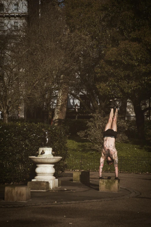 a person doing a handstand in a park, by Lee Gatch, square, tattooed, photographic, scene