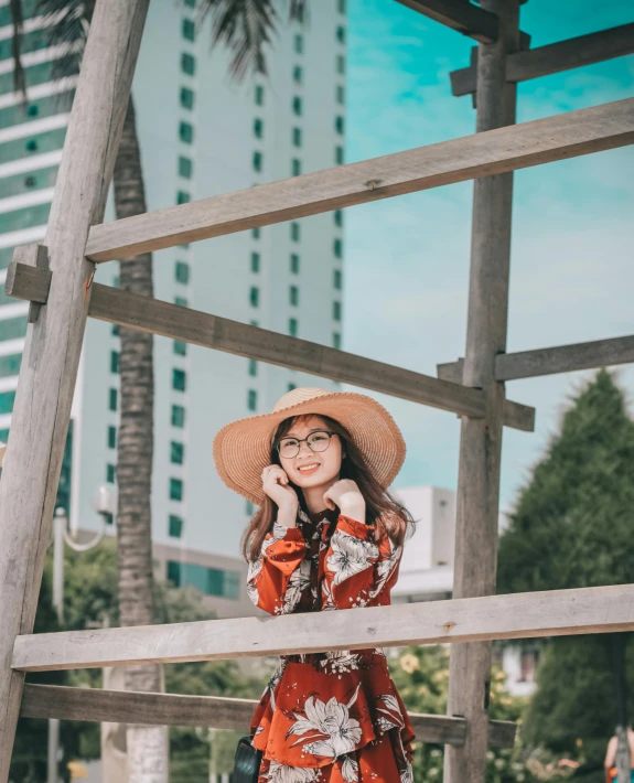 a woman in a hat talking on a cell phone, inspired by Cheng Jiasui, pexels contest winner, standing astride a gate, wearing a red sundress, set on singaporean aesthetic, posing for a picture