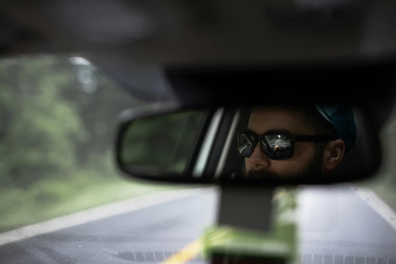 a man taking a picture of himself in a rear view mirror, by Andrew Domachowski, bearded, rally driving photo, wearing shades, **cinematic