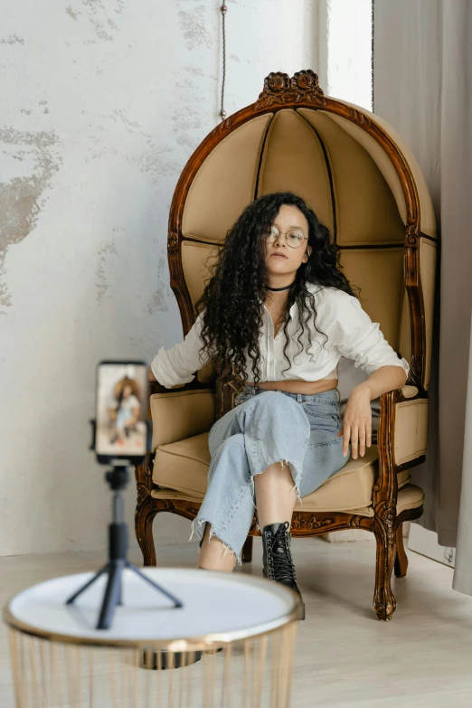 a woman sitting in a chair in a room, trending on pexels, renaissance, long wild black curly hair, smartphone photo, tripod, non binary model