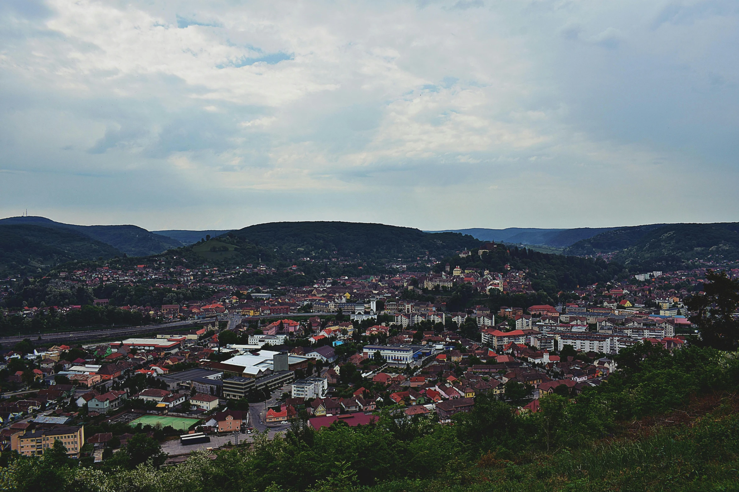 a view of a city from the top of a hill, by Emma Andijewska, black forest, square, cinematic, lo-fi