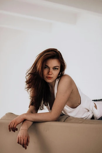 a beautiful young woman laying on top of a bed, by Ivan Grohar, unsplash, auburn hair, sitting on the couch, on a pale background, фото девушка курит