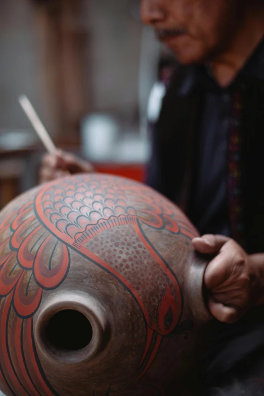 a man that is sitting down with a vase, a detailed painting, trending on unsplash, wearing shipibo tattoos, bowl, in a workshop, eagle feather