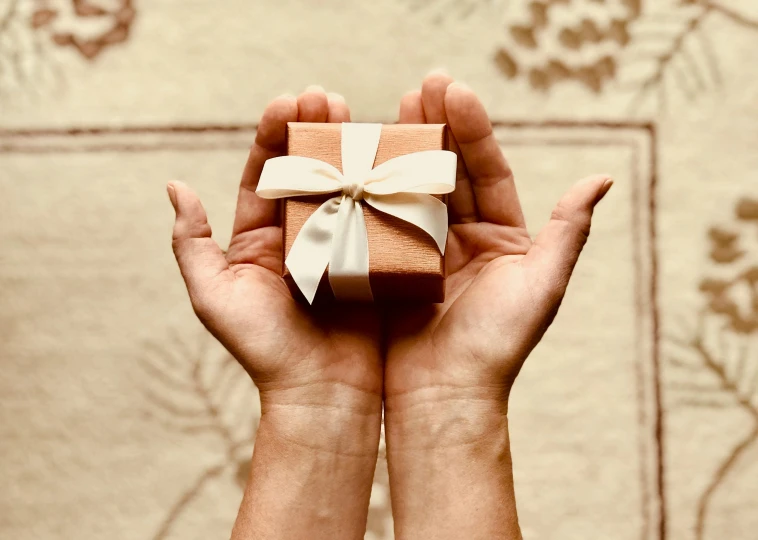 a person holding a small gift in their hands, by Emma Andijewska, pexels contest winner, renaissance, ivory and copper, skincare, thick bow, thumbnail