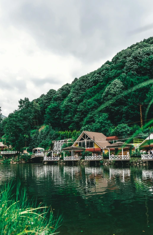 a body of water next to a lush green hillside, sumatraism, peaceful wooden mansion, woodland village, boat dock, festivals