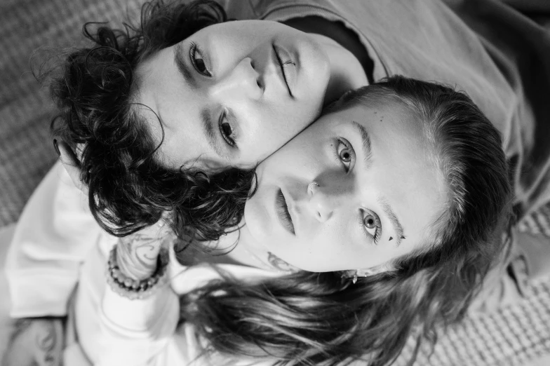 a couple of people laying on top of a bed, a black and white photo, pexels, antipodeans, androgynous face, sisters, high angle closeup portrait, portrait shot 8 k