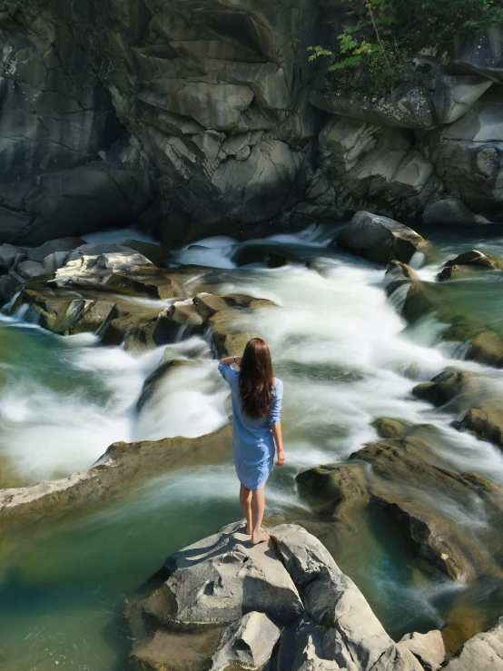 a woman standing on top of a rock next to a river, river rapids, cindy avelino, multiple stories, tourism