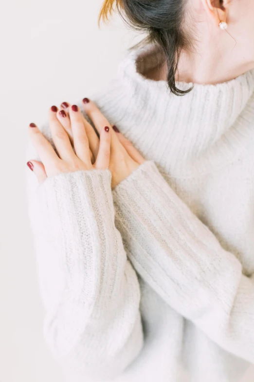 a woman with her hands on her chest, trending on pexels, white sweater, pale red, maroon, designed for cozy aesthetics!