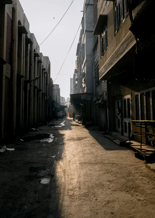 a man walking down a street next to tall buildings, a detailed matte painting, by Ibrahim Kodra, unsplash contest winner, old jeddah city alley, shafts of sunlight in the centre, iraq nadar, quiet street