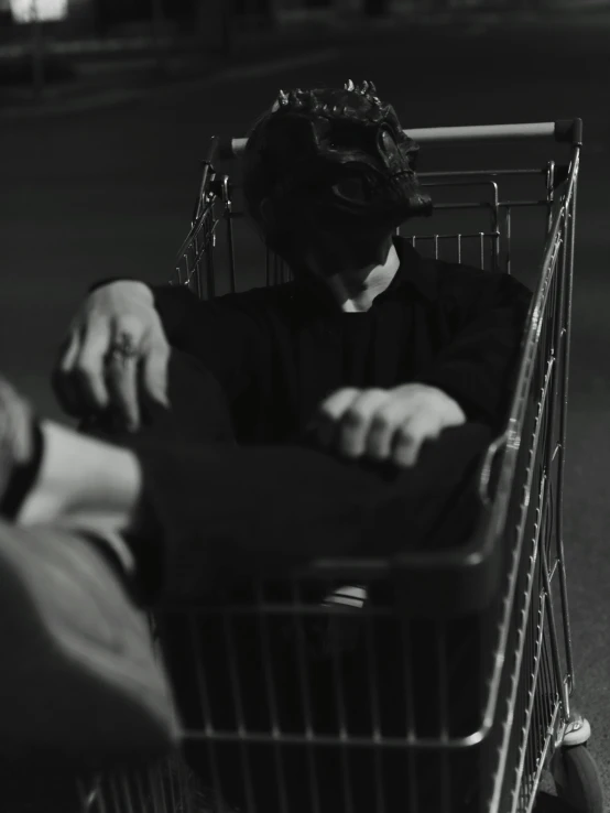 a black and white photo of a person sitting in a shopping cart, by Adam Rex, faceless people dark, still from a live action movie, black clothing, sleepy