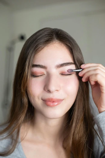 a woman is putting eyeliners on her eyes, a colorized photo, inspired by Lilia Alvarado, trending on pexels, soft shadow, eyes half closed, smooth oval shape face, on white