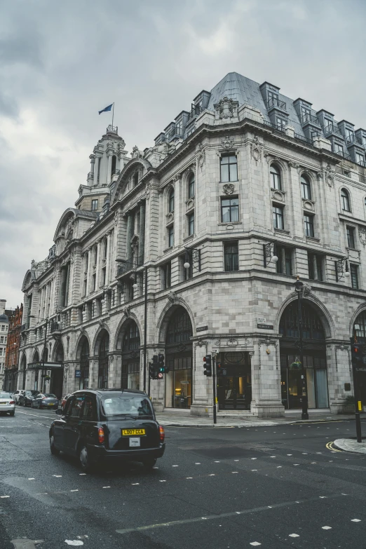 a car driving down a street next to a tall building, by Nina Hamnett, pexels contest winner, art nouveau, victorian london, stone facade, stores, neoclassical tower with dome