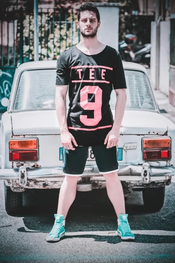 a man standing in front of a parked car, by Telemaco Signorini, pexels contest winner, wearing shorts and t shirt, rated t for teen, 9 9 designs, pink and black