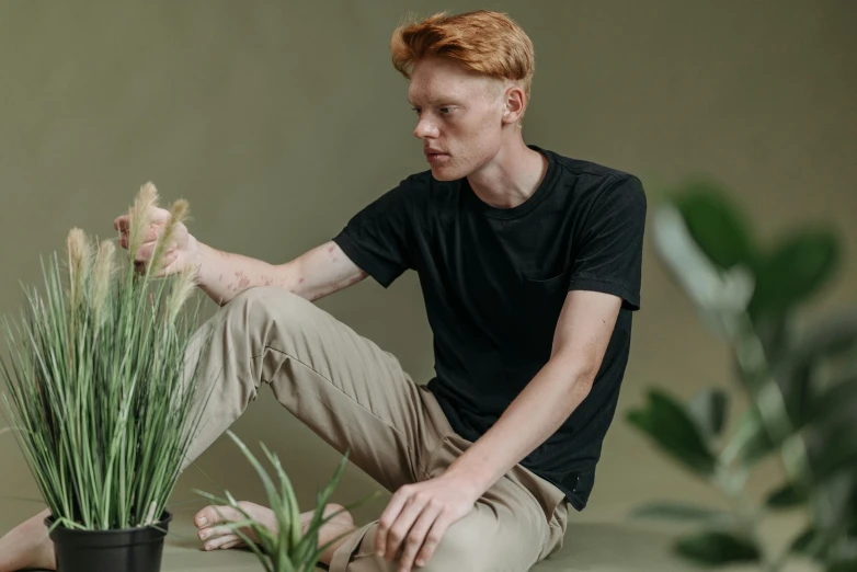 a man sitting on the ground next to a potted plant, pexels contest winner, he is wearing a black t-shirt, ginger hair, olive green slacks, very very very pale skin