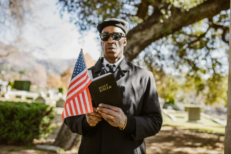 a man holding a bible and an american flag, an album cover, pexels contest winner, graveside, black people, dressed like in the 1940s, bay area