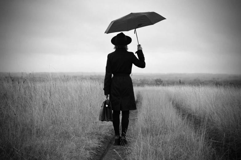 a black and white photo of a woman holding an umbrella, unsplash, conceptual art, black stetson and coat, in the countryside, walking to work with a briefcase, recital