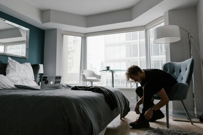 a man putting on his shoes in a bedroom, by Adam Rex, pexels contest winner, floor - to - ceiling windows, bo burnham, alana fletcher, dylan kowalsk