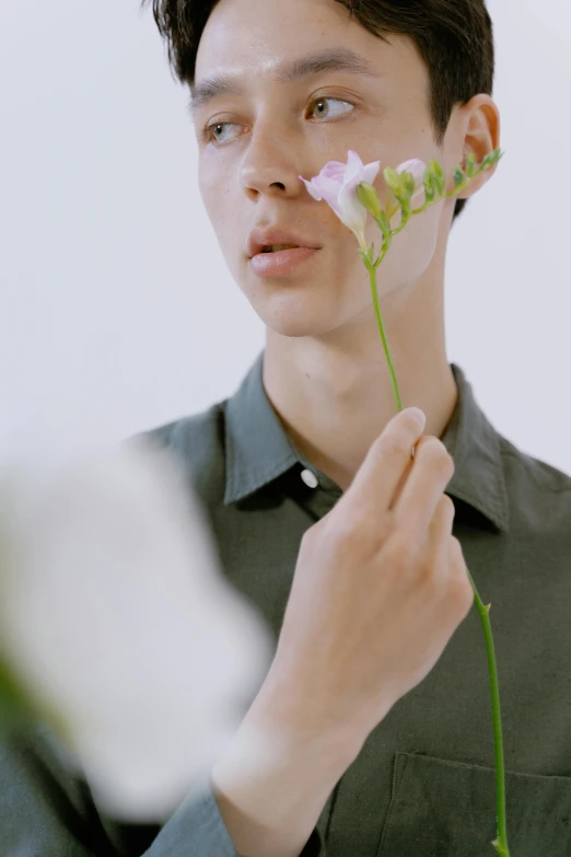 a man holding a flower in front of his face, an album cover, inspired by Fei Danxu, aestheticism, nonbinary model, wearing polo shirt, (aesthetics), detail shot