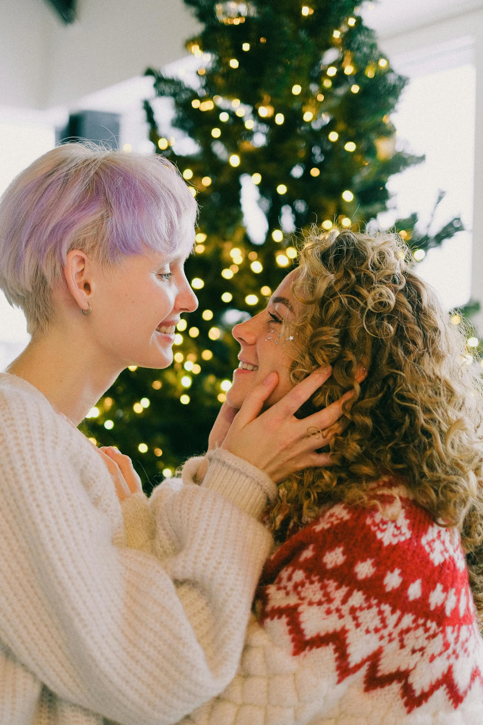 two women standing next to each other in front of a christmas tree, trending on pexels, lilac hair, lesbian embrace, curly, gif