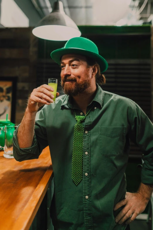 a man standing at a bar holding a drink, wearing green clothing, irish genes, jack black, 🍸🍋