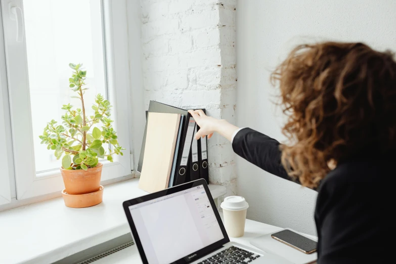 a woman sitting at a desk in front of a laptop, pexels contest winner, private press, pointing index finger, clean minimalist design, standing in corner of room, stacked image