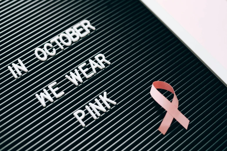 a pink ribbon sitting on top of a letter board, october, white wearing, michael welan, wear and tear