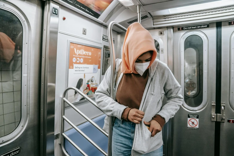 a woman wearing a face mask on a subway, trending on unsplash, graffiti, white hijab, long orange sweatshirt, in the middle of new york, exiting from a wardrobe