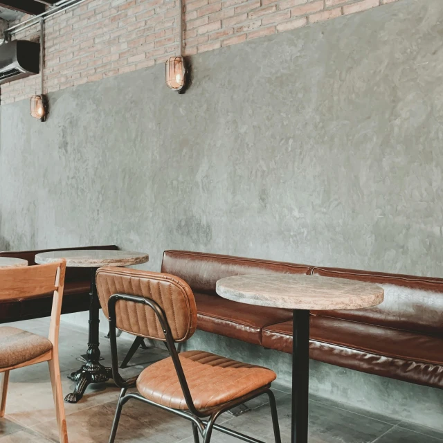 a table and some chairs in a room, trending on pexels, concrete wall, leather padding, in a coffee shop, thumbnail