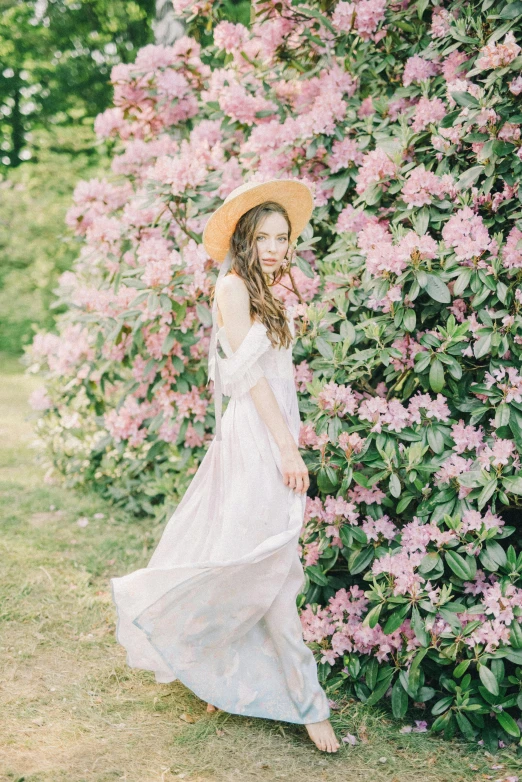 a woman standing in front of a bush of flowers, inspired by Oleg Oprisco, unsplash, high quality photo, white and pink, wearing wide sunhat, low quality photo