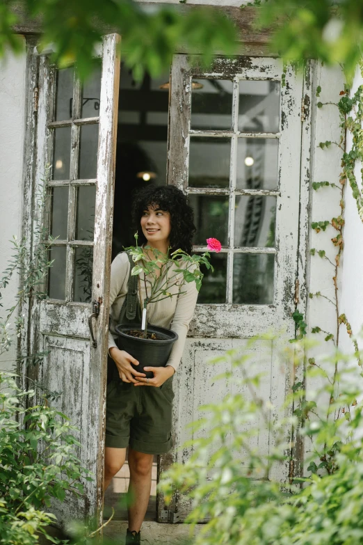 a woman standing in the doorway of a house, inspired by Yuko Tatsushima, pexels contest winner, renaissance, in bloom greenhouse, dark short curly hair smiling, thawan duchanee, with a tall tree