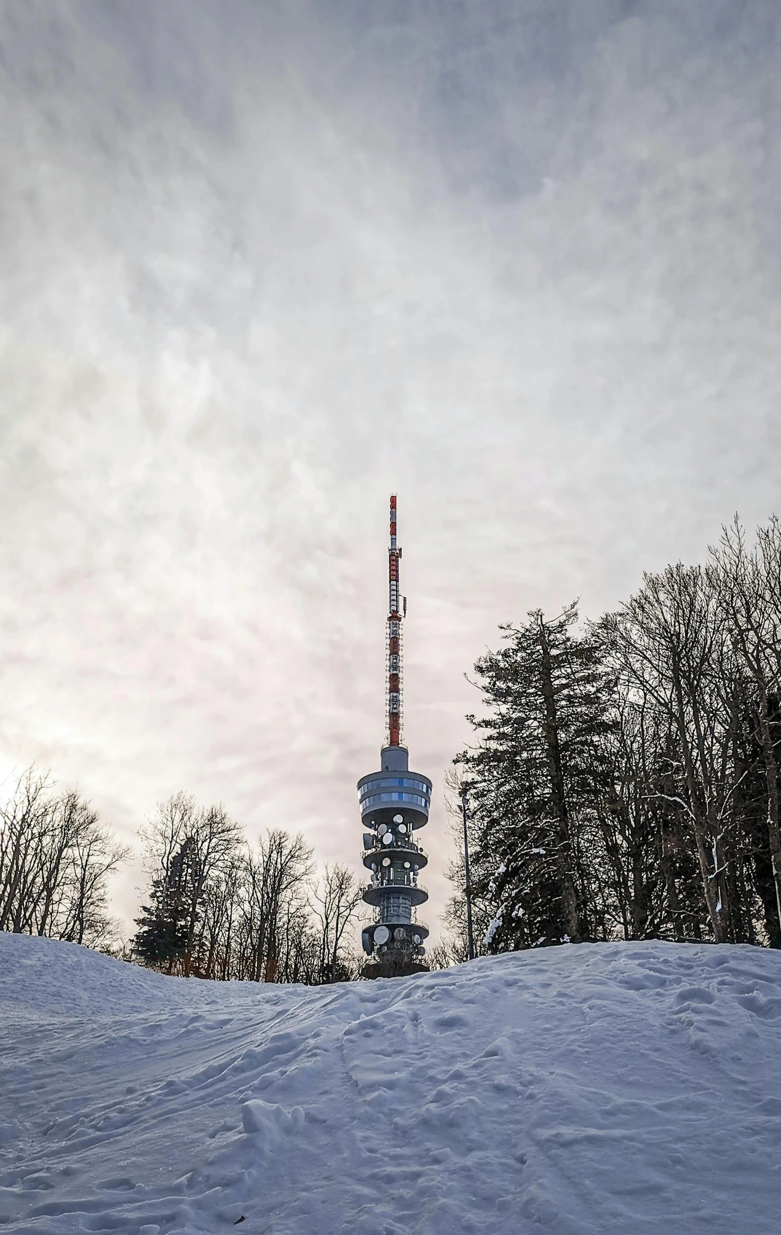 a snow covered hill with a radio tower in the background, by Adam Marczyński, 4k press image, tourist photo, near forest, tall building