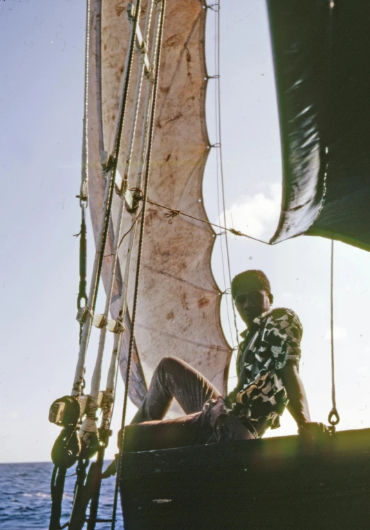 a man sitting on top of a boat in the ocean, by Robert Jacobsen, hurufiyya, 1960s color photograph, sails and masts and rigging, masai, close - up photograph