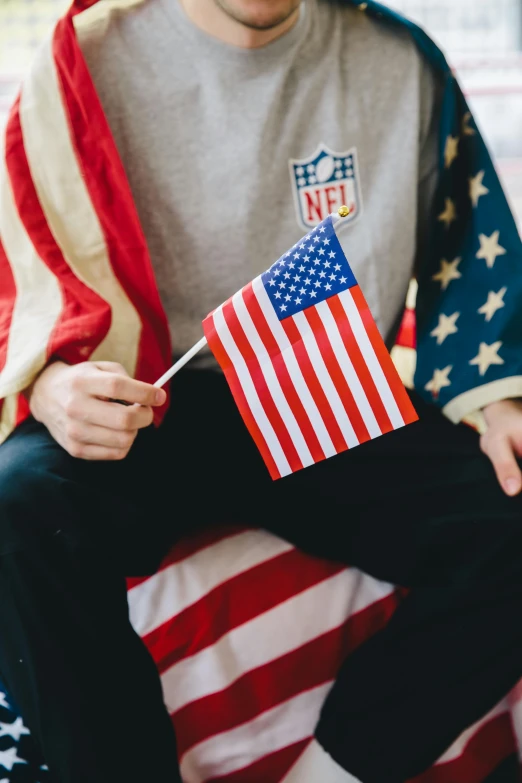 a man sitting on a bed holding an american flag, trending on unsplash, holding a football, flags, 🚿🗝📝, holding court