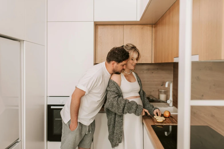 a man standing next to a woman in a kitchen, by Adam Marczyński, pexels contest winner, third trimester, blonde, comfortable, background image