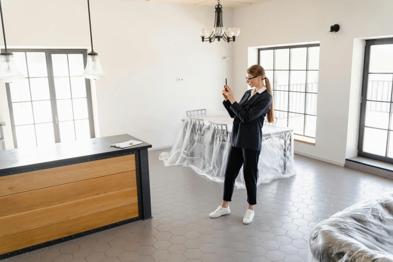 a woman standing in a room holding a cell phone, architectural planning, inspect in inventory image, furniture around, black floor