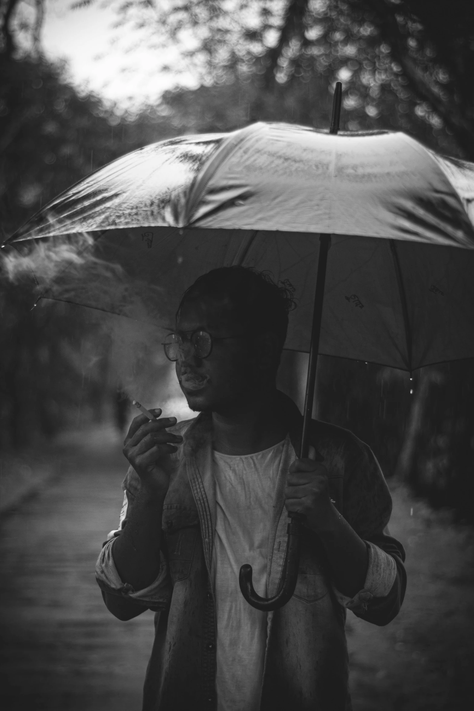 a black and white photo of a man holding an umbrella, a black and white photo, by Basuki Abdullah, smoking a cigarrette🚬, dark-skinned, lofi hip hop, single person with umbrella