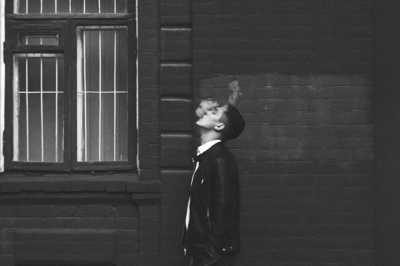 a black and white photo of a man smoking a cigarette, a black and white photo, by Emma Andijewska, pexels, purism, leaning on the wall, dressed in leather jacket, dreaming of kissing a girl, short hair on top of his head