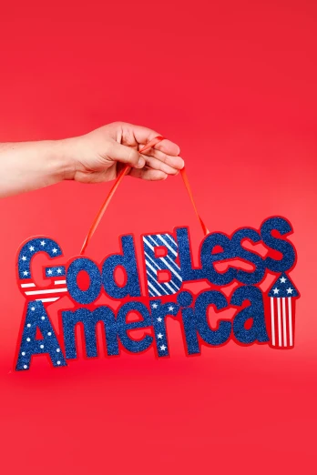 a person holding a sign that says god bless america, pexels contest winner, glitter accents on figure, a brightly colored, flowing lettering, official product photo