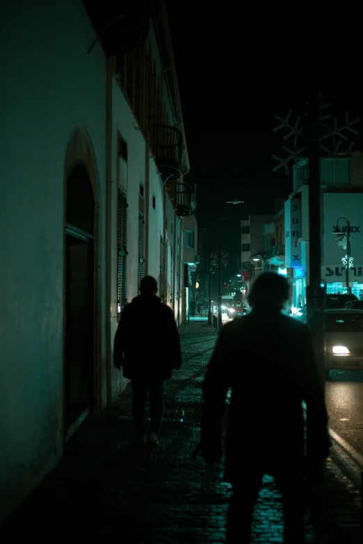 a couple of people walking down a street at night, teal lights, abandoned streets, 8 k movie still