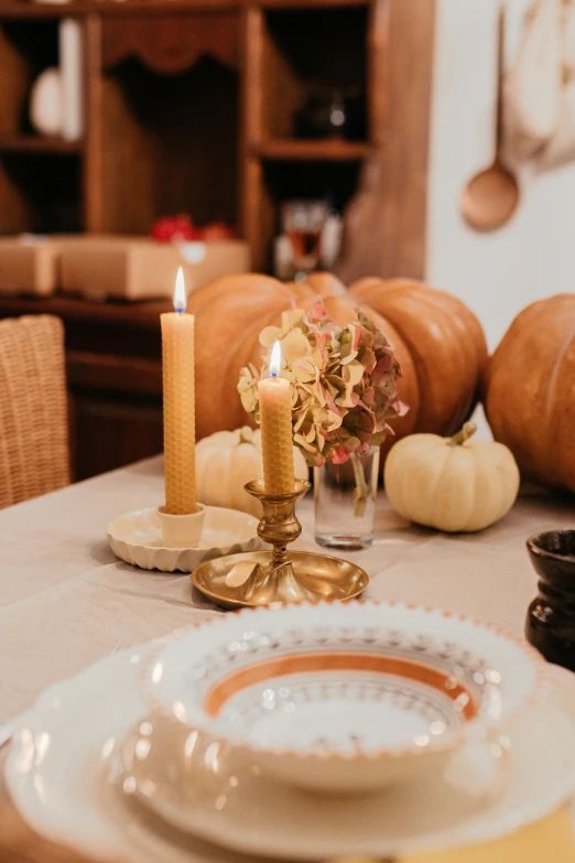 a white plate sitting on top of a table next to a candle, gourds, indoor, gold accessories, profile image