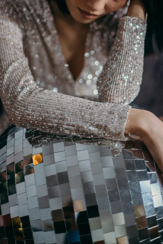 a woman sitting on top of a disco ball, an album cover, by Nina Hamnett, trending on pexels, luxury dress, detail shot, long sleeves, grey