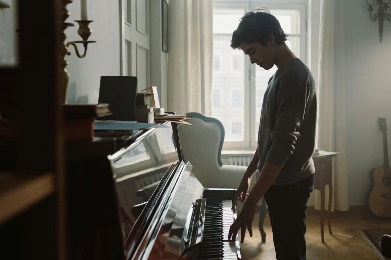 a man standing next to a piano in a living room, by Tobias Stimmer, pexels contest winner, avan jogia angel, standing near a window, hammershøi, music being played