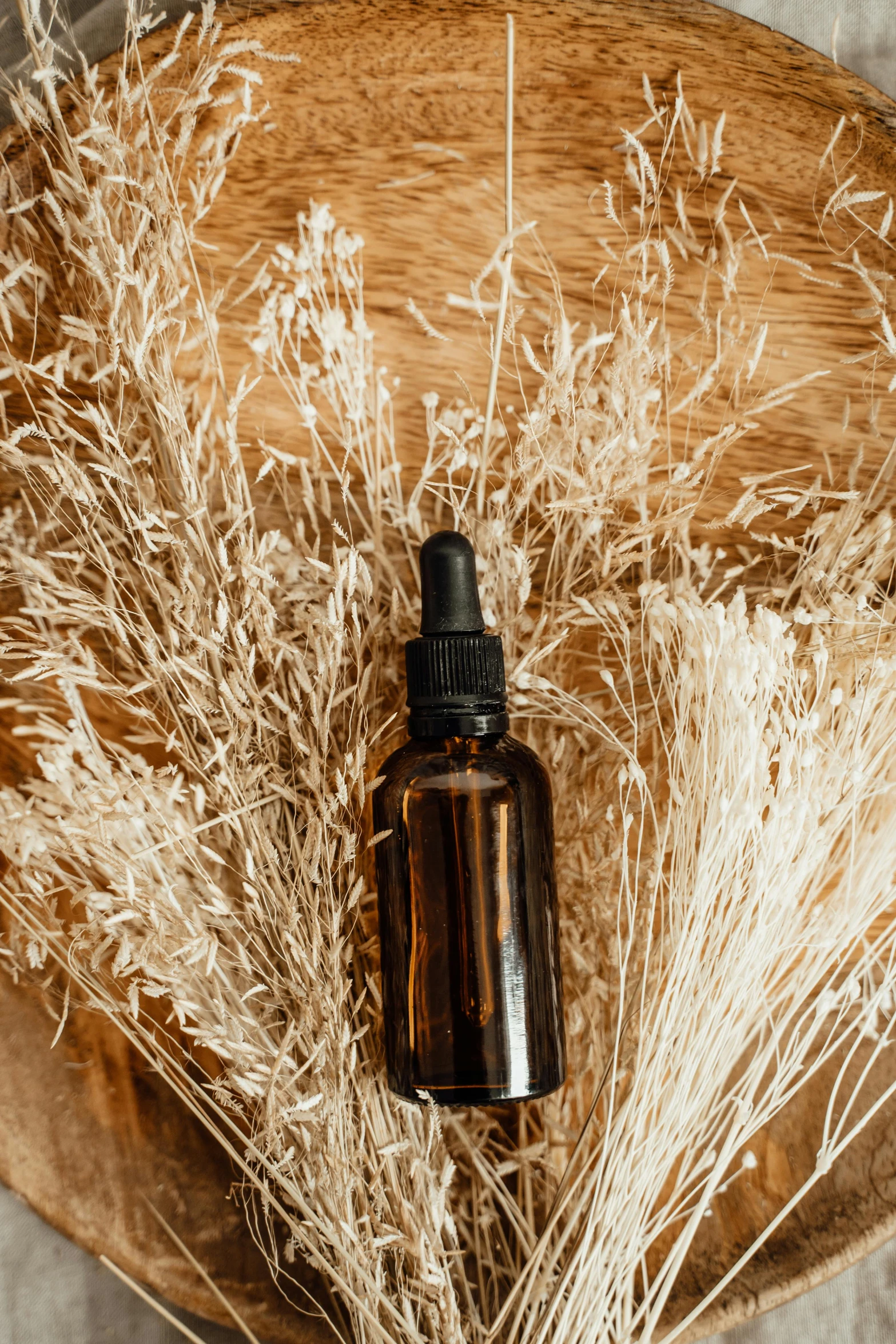 a bottle of essential oil sitting on top of a wooden bowl, by Andries Stock, trending on pexels, renaissance, dry grass, black fine lines on warm brown, photoshoot for skincare brand, thumbnail