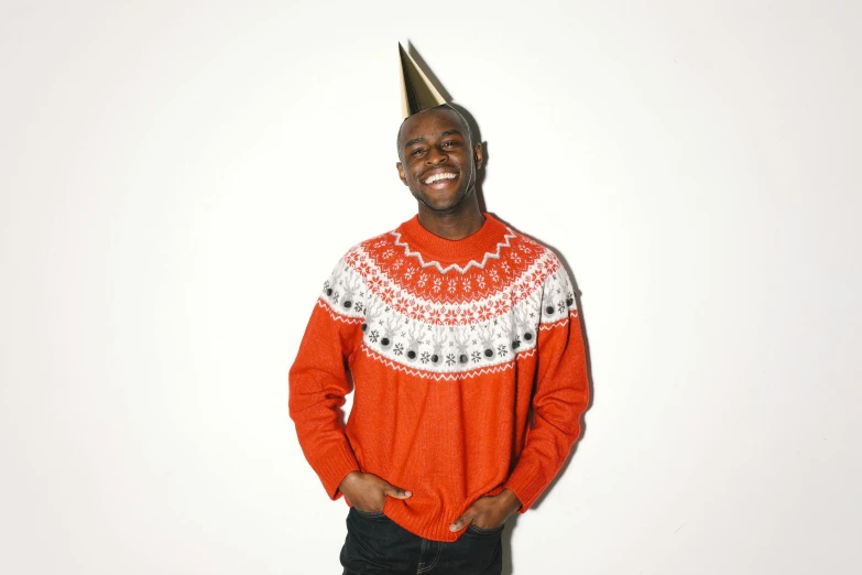a man wearing a party hat standing in front of a white wall, an album cover, inspired by Ernest William Christmas, he is wearing a brown sweater, kevin hart, catalog photo, super high resolution