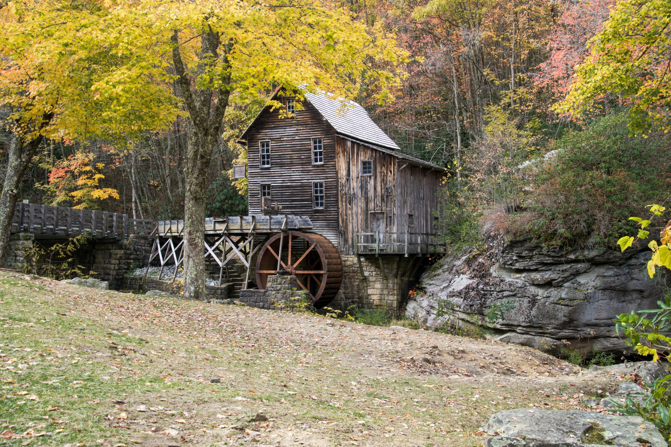 a wooden building sitting on top of a lush green hillside, by Dan Frazier, pexels contest winner, renaissance, water wheel, muted fall colors, tn, panoramic
